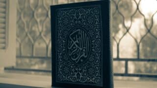 Decorative book cover with Arabic script and floral patterns by a window with metal grille.