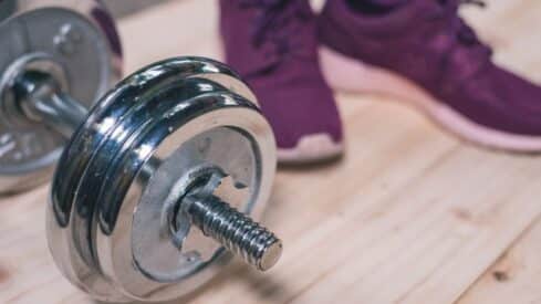 Chrome dumbbell on light wood surface with purple athletic shoes nearby.