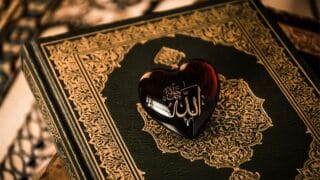 Decorative book with intricate cover and heart-shaped object with Arabic script on top.