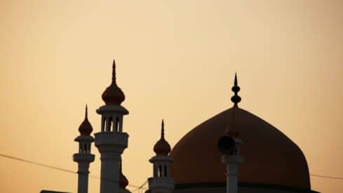 Silhouette of a mosque with minarets and domes against a sunset sky.