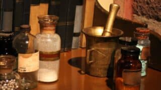 Wooden table with glass bottles, metal mortar and pestle, books in background.