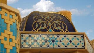 Building with ornate dome, golden patterns, blue and yellow tiles against clear sky.