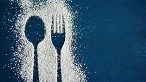 Spoon and fork silhouette on blue background with sprinkled white powder.