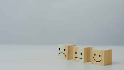 Three wooden cubes with sad, neutral, and happy faces on a light surface.