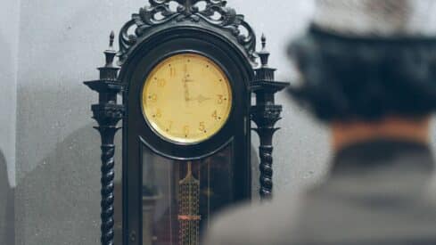 Ornate wooden grandfather clock with yellow face, intricate carvings, blurred figure in foreground.