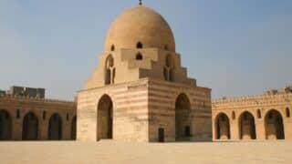 Large historic mosque with stone dome, striped archways, open courtyard, Middle Eastern style.