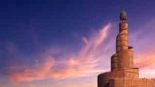 Spiral minaret with helical design against pink and purple clouds at sunset or sunrise.