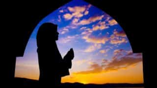 Silhouette of a person praying under an archway with a colorful sunset sky and clouds.