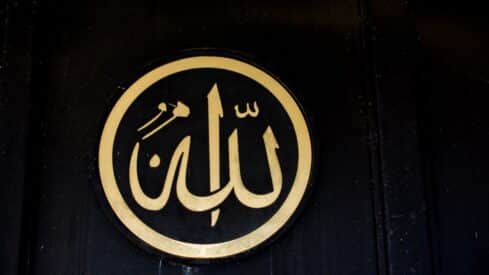 Circular emblem with word of Allah in gold Arabic calligraphy on black background.