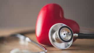 Stethoscope beside red heart object on wooden surface, symbolizing health and cardiology.