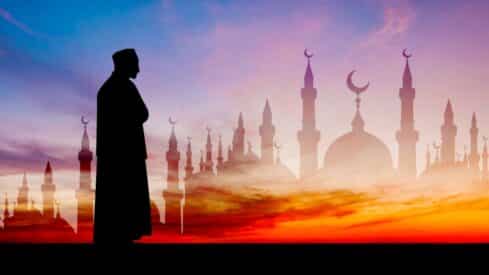 Silhouette of a person before mosque with minarets and sunset sky, creating a serene scene.