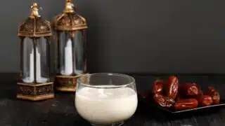 Glass of creamy drink with dates and ornate lanterns on a dark surface.