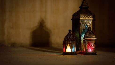 Three decorative lanterns with red, blue, and yellow glass on a surface against a plain wall.