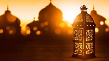 Decorative lantern with patterns, illuminated against blurred domed structures at sunset.