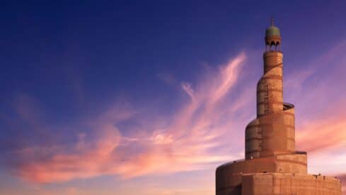 Spiral mosque minaret with geometric patterns at sunset, blue and pink sky, green dome on top.