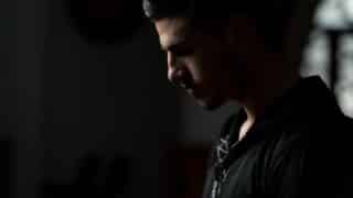 Young man in profile, dimly lit, wearing black shirt, contemplative expression with shadows.