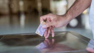 Person inserting banknote into slot on metallic surface, possibly for donation or payment.