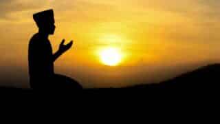 Silhouette of a kneeling person with raised hands against a vibrant sunset sky.