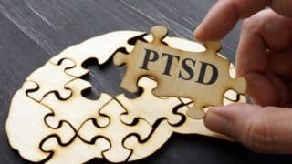 Wooden brain jigsaw puzzle with a hand fitting a PTSD piece.