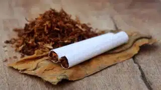 Hand-rolled cigarette and loose tobacco on a leaf on wooden surface.