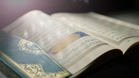 Open holy Quran with Arabic script and decorative motifs in soft lighting.