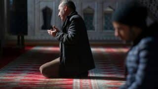 Man kneeling on red carpet in prayer inside ornately decorated building with soft lighting.