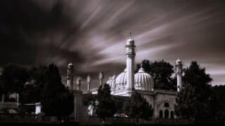 Large mosque with domes and minarets, dramatic sky, trees, black and white rendering.