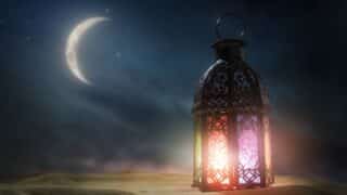 Decorative lantern with colorful light and night sky, crescent moon, stars, and sand dunes.