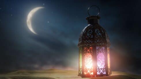 Decorative lantern with colorful light and night sky, crescent moon, stars, and sand dunes.