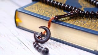 Ornate blue and gold holy Quran with a string of beads ending in a crescent moon and star.