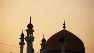 Silhouette of a mosque at dusk with a large dome and multiple minarets against the sky.