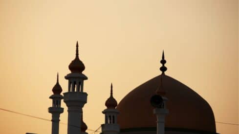 Silhouette of a mosque at dusk with a large dome and multiple minarets against the sky.