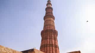 Tall stone minaret with red sandstone and balcony, clear sky, bird to the right.