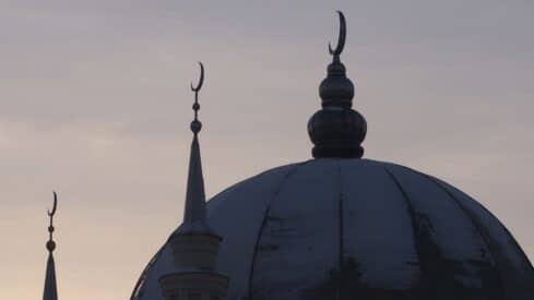 Mosque silhouette with dome and minarets against a dusky sky, featuring crescent moon finials.