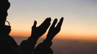 Silhouette of person raising hands against a gradient sunrise or sunset sky.