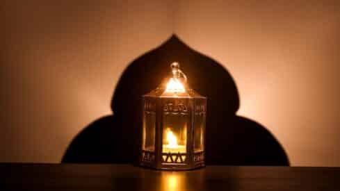 Decorative lantern with lit candle casting an ornate arch-shaped shadow on the wall.