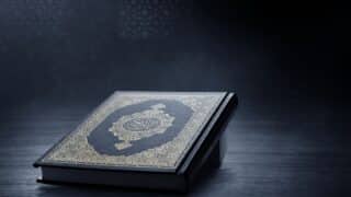 Closed holy Quran with ornate cover and Arabic script on a dark background.