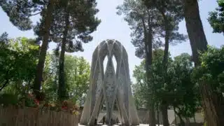 Intricately designed monument amidst trees and flowers in a sunny outdoor setting.