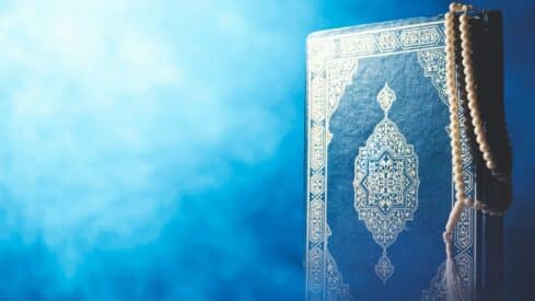 Ornate Quran with prayer beads draped over corner, set against a blue background.