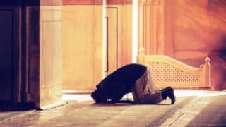 Person kneeling in prayer in warmly lit ornate interior with light streaming through entrance.