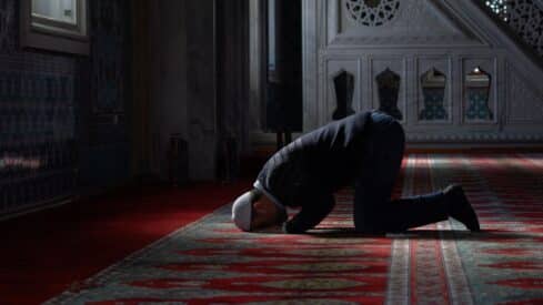 Person kneeling on red carpet in dimly lit space with intricate decor and arched windows.