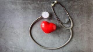 Stethoscope encircles a red heart on textured gray background, symbolizing heart health.