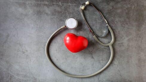 Stethoscope encircles a red heart on textured gray background, symbolizing heart health.