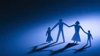 Silhouette of a paper cutout family of four holding hands on a blue gradient background.