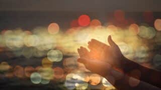 Two open hands with blurred bokeh circular lights in a warm, glowing background.