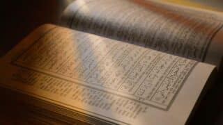 An open page of the Holy Qur'an with a lighted Qur'anic text.