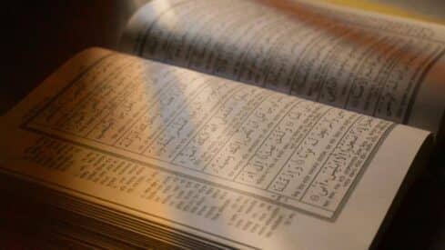 An open page of the Holy Qur'an with a lighted Qur'anic text.