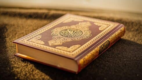 Decorative hardcover of Quran with gold patterns and Arabic script on a dark surface.