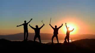 Silhouetted figures on a hilltop at sunset with colorful sky and distant mountains.