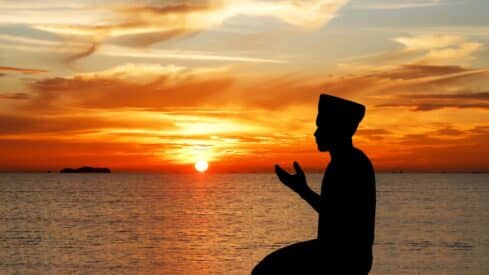 Silhouette of a person contemplating a sunset over a calm ocean with orange and yellow clouds.